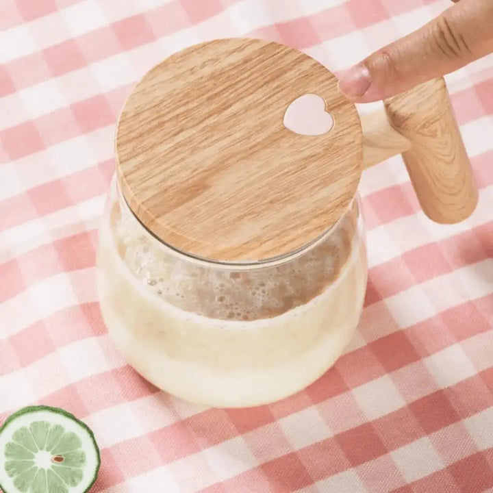 Glaskrug mit Holzdeckel und Herz, gefüllt mit Milchshake, auf rosa-weiß kariertem Tuch.