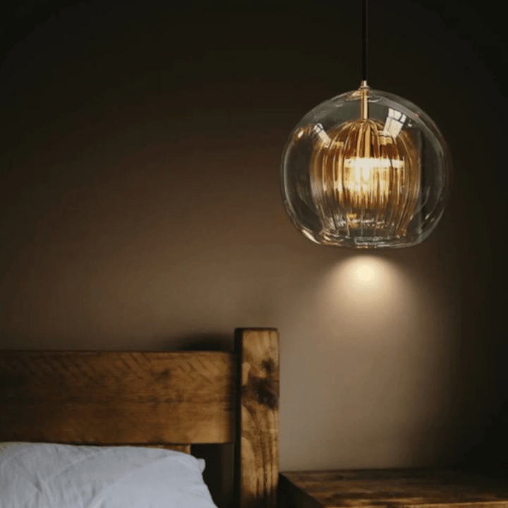 Kugelförmige Glaspendelleuchte über rustikalem Holzbett, warmes Licht, modernes Design.