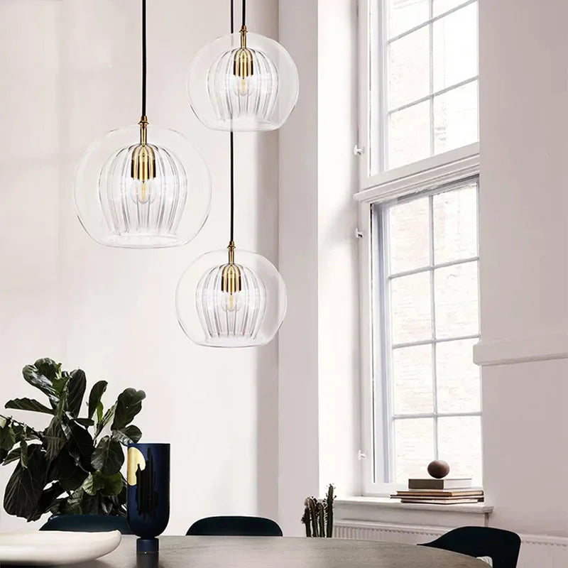 Drei moderne Glaspendelleuchten, goldene Details, hängend in minimalistischem Esszimmer.