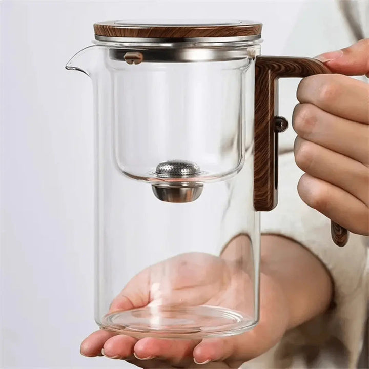 Glas-Teekanne mit Holzgriff, Edelstahlfilter, modernes Design, transparent, handgehalten.