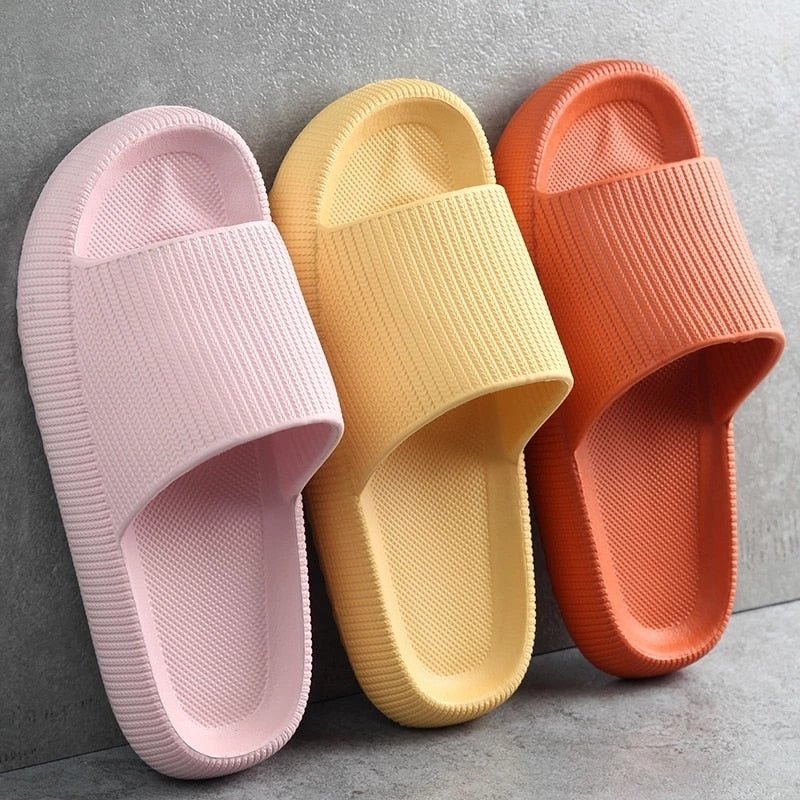 Drei bunte Pantoletten aus Gummi in Rosa, Gelb und Orange auf grauem Hintergrund.
