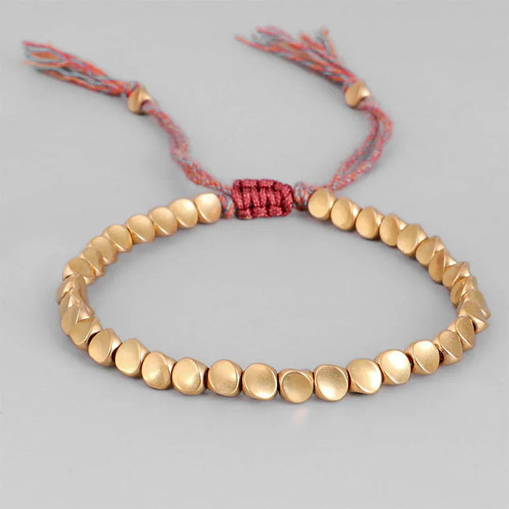 Goldfarbenes Armband mit runden Perlen und verstellbarem roten Kordelverschluss.