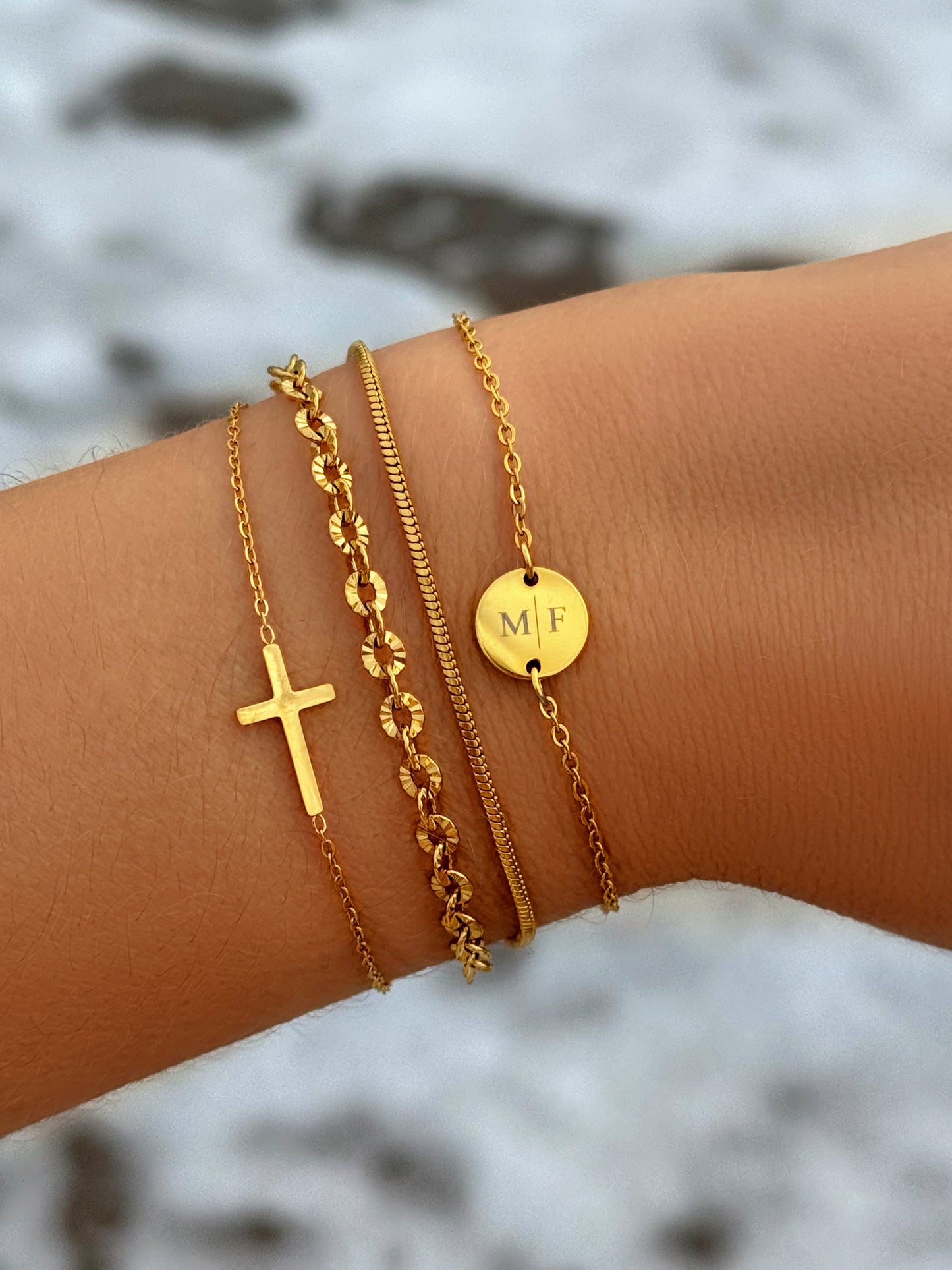 Goldene Armbänder-Set mit Kreuz und Initialen-Anhänger auf Handgelenk, modischer Schmuck.