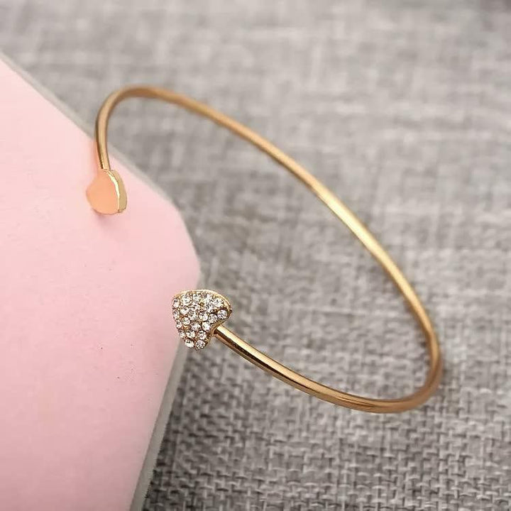 Goldenes Armreif mit Herzanhänger, funkelnde Strasssteine, elegantes Schmuckdesign.