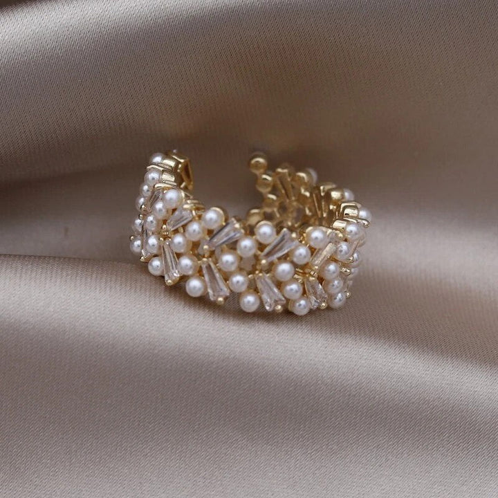 Goldener Ring mit Perlen und Kristallen auf beigem Stoff, eleganter Schmuck für Damen.