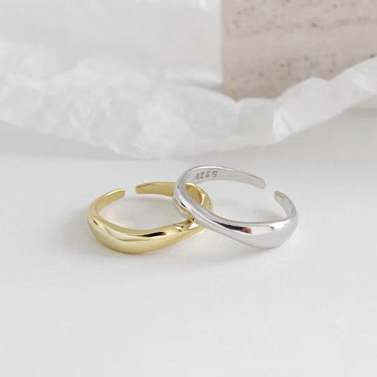 Zwei offene Ringe aus Gold und Silber auf weißem Hintergrund, minimalistisch, modern.