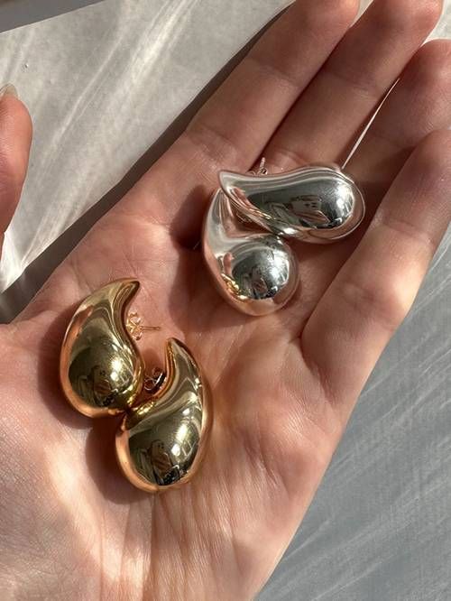 Goldene und silberne Tropfen-Ohrringe, glänzend, modern, in Hand gehalten.