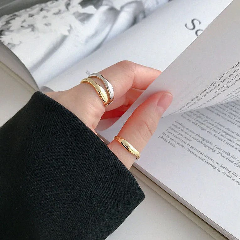 Hand mit goldenen und silbernen Ringen blättert Buch um, eleganter Schmuck, minimalistisch.