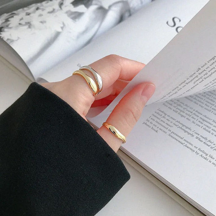Hand mit goldenen und silbernen Ringen blättert Buch um, eleganter Schmuck, minimalistisch.