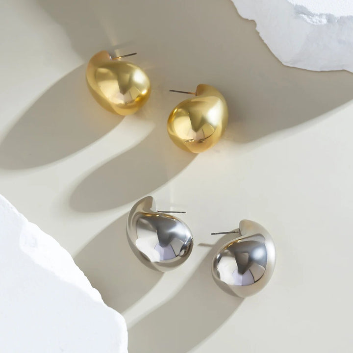 Goldene und silberne Ohrringe, tropfenförmig, glänzend, auf hellem Hintergrund.