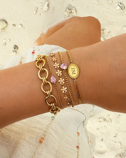 Goldene Armbänder-Set mit rosa Details am Handgelenk auf Sandhintergrund.