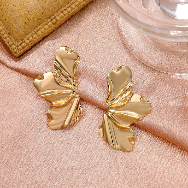 Goldene, blattförmige Ohrringe auf rosa Stoff, eleganter Schmuck, modisches Accessoire.