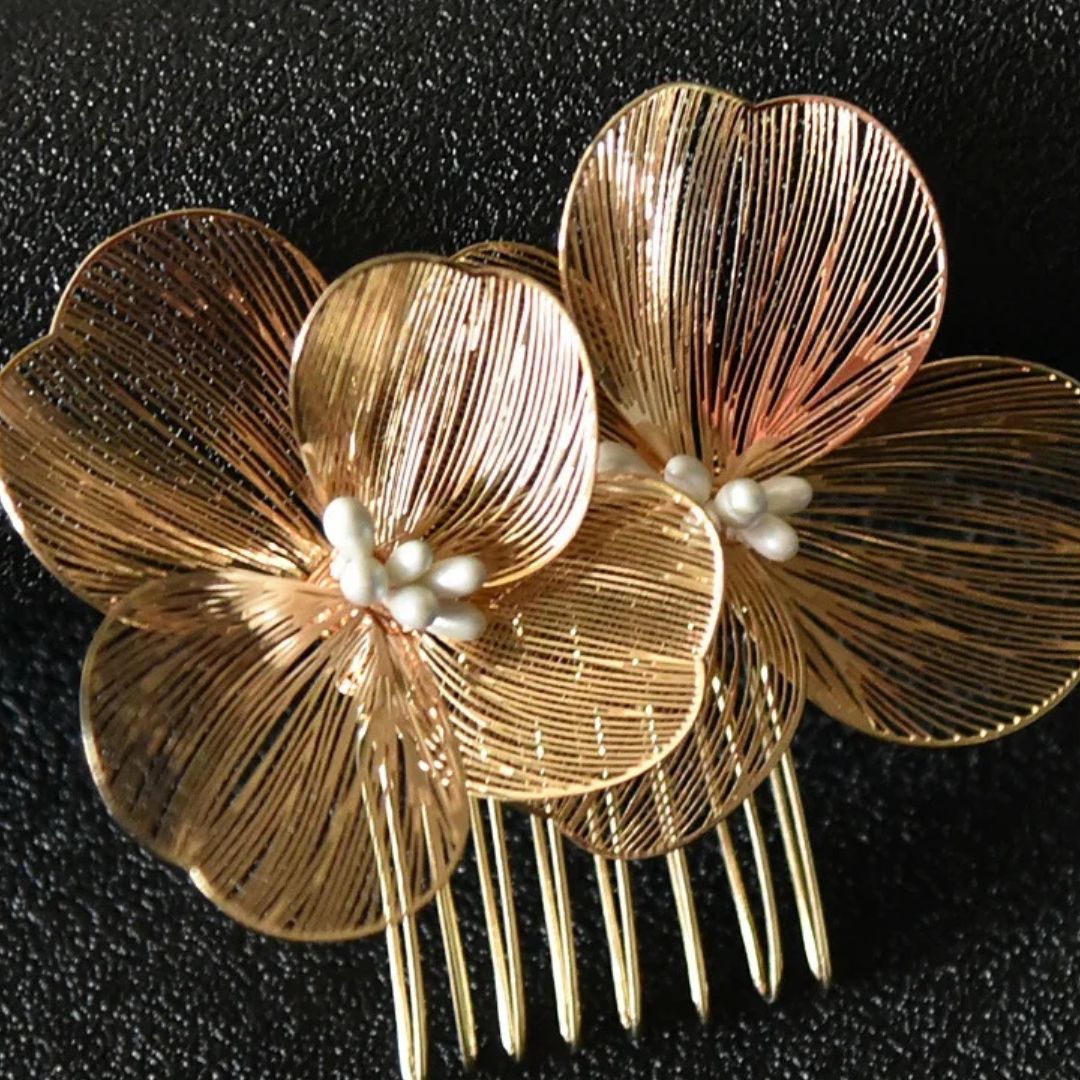 Goldene Haarspange mit Blumenmotiv, filigranem Design und Perlendetails auf schwarzem Hintergrund.
