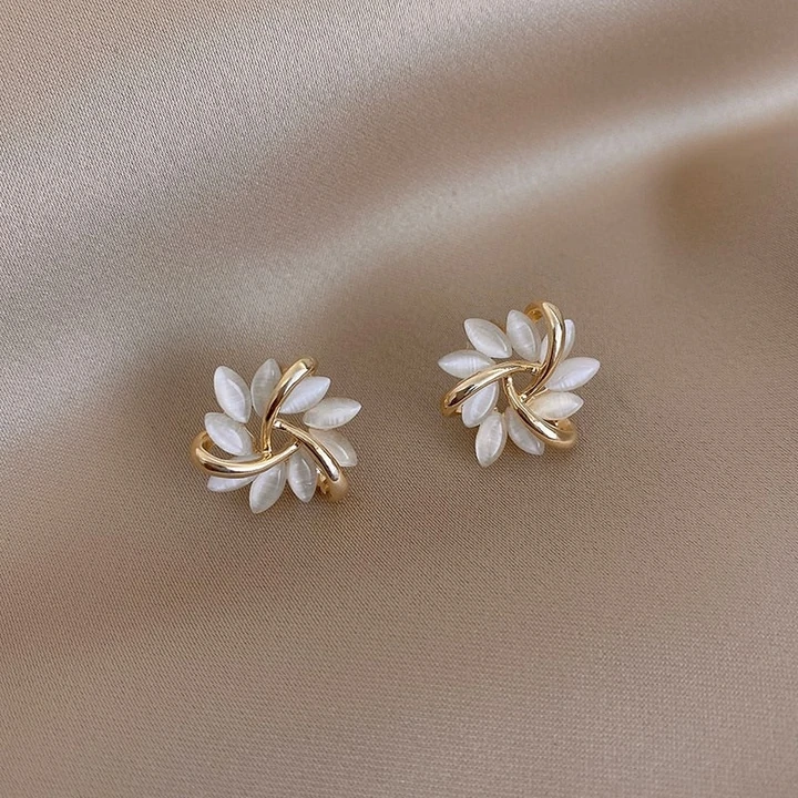 Goldene Ohrringe mit Perlmuttblättern auf beigem Stoff, eleganter Schmuck, Damenaccessoire.