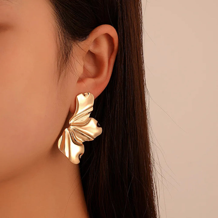 Goldene, blattförmige Ohrringe an Ohr, modisches Accessoire, eleganter Schmuck, Damenmode.
