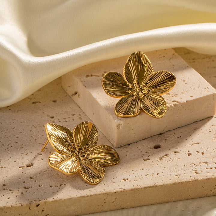 Goldene Blumen-Ohrringe auf Stein, eleganter Schmuck, luxuriöses Design, Damenaccessoire.