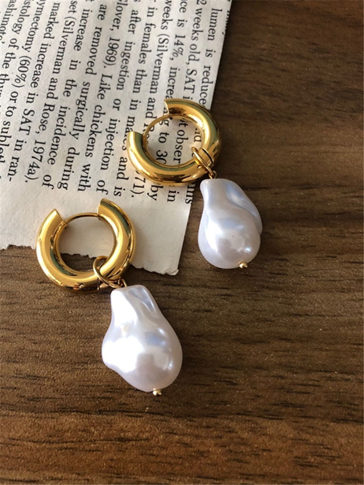 Goldene Creolen mit weißen Barockperlen, eleganter Schmuck, Holzuntergrund.