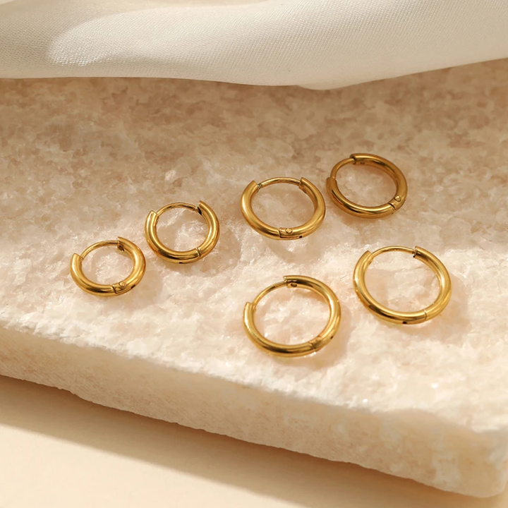 Goldene Creolen-Ohrringe auf Marmor, eleganter Schmuck, modische Accessoires, Damenmode.