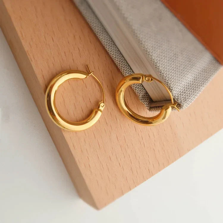 Goldene Creolen Ohrringe auf Holzuntergrund, eleganter Schmuck, modisches Accessoire.