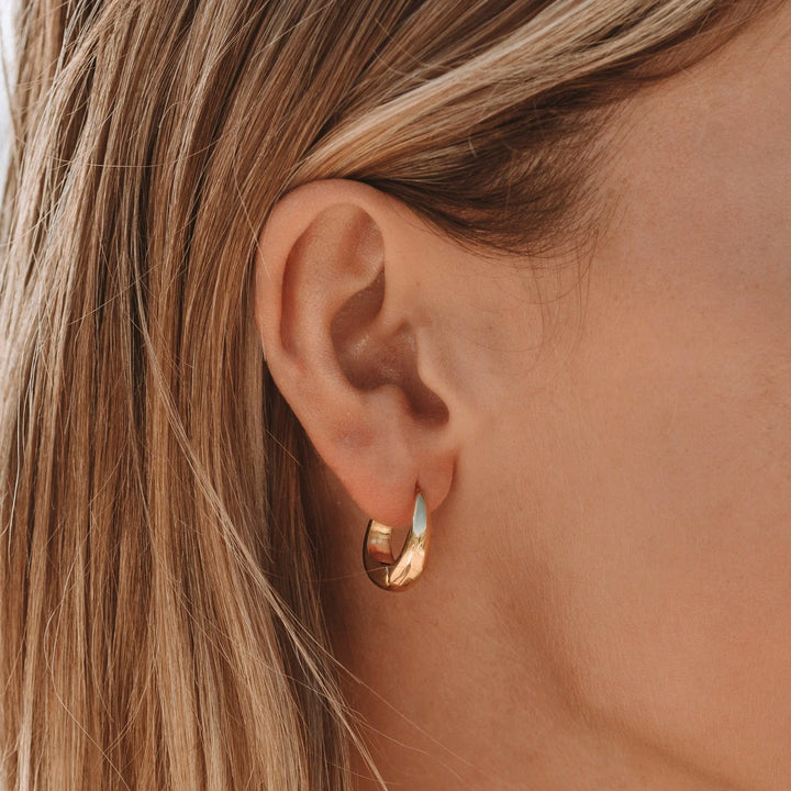 Goldene Creolen-Ohrringe an Ohr, eleganter Schmuck, modisches Accessoire, Damenmode.