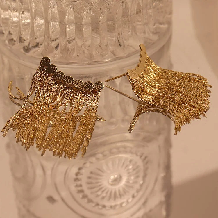 Goldene Quasten-Ohrringe auf Glasoberfläche, eleganter Schmuck, modisches Accessoire.