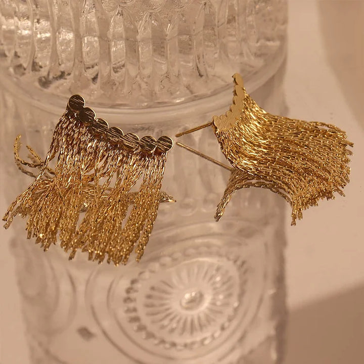 Goldene Quasten-Ohrringe auf Glasoberfläche, eleganter Schmuck, modisches Accessoire.