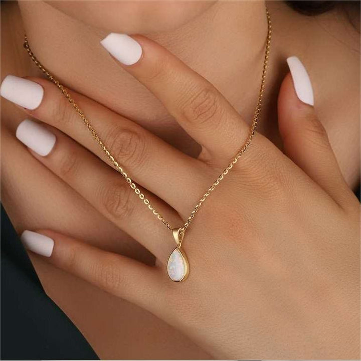 Frau mit goldener Halskette und Opal-Anhänger, elegante Maniküre, Schmuckmode.