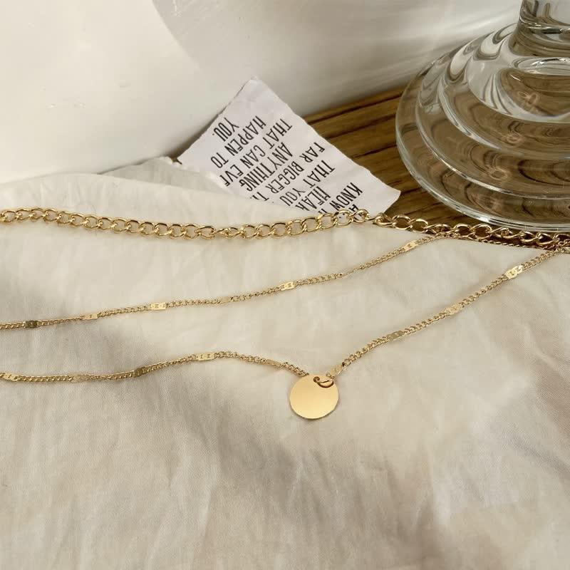 Goldene Halskette mit rundem Anhänger auf weißem Stoff, eleganter Schmuck, Damenaccessoire.