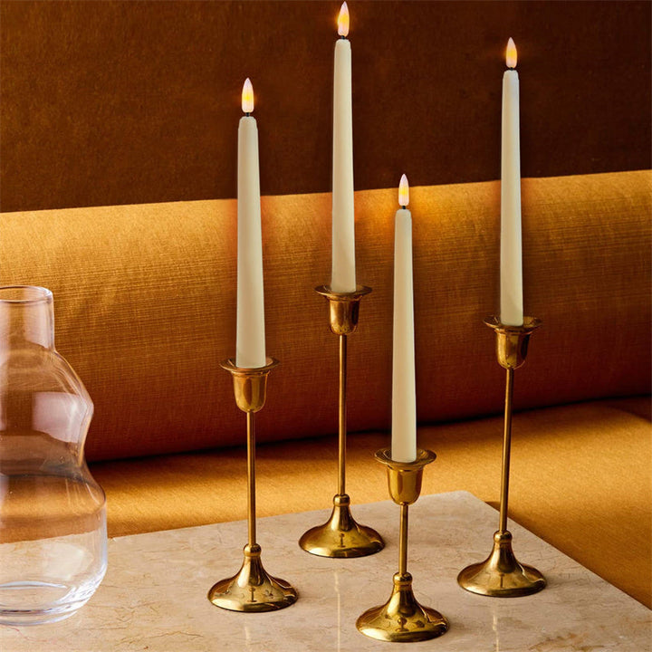 Vier goldene Kerzenhalter mit weißen Kerzen auf Marmortisch, elegantes Wohnaccessoire.