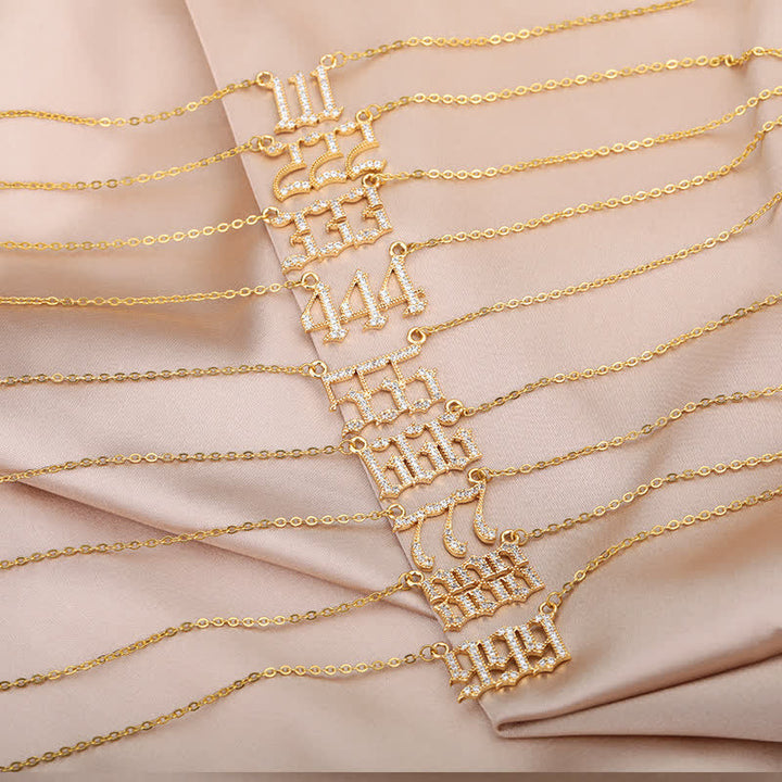 Goldene Armbänder mit Zahlenanhängern auf beigem Stoff, Schmuck, modisch, elegant.