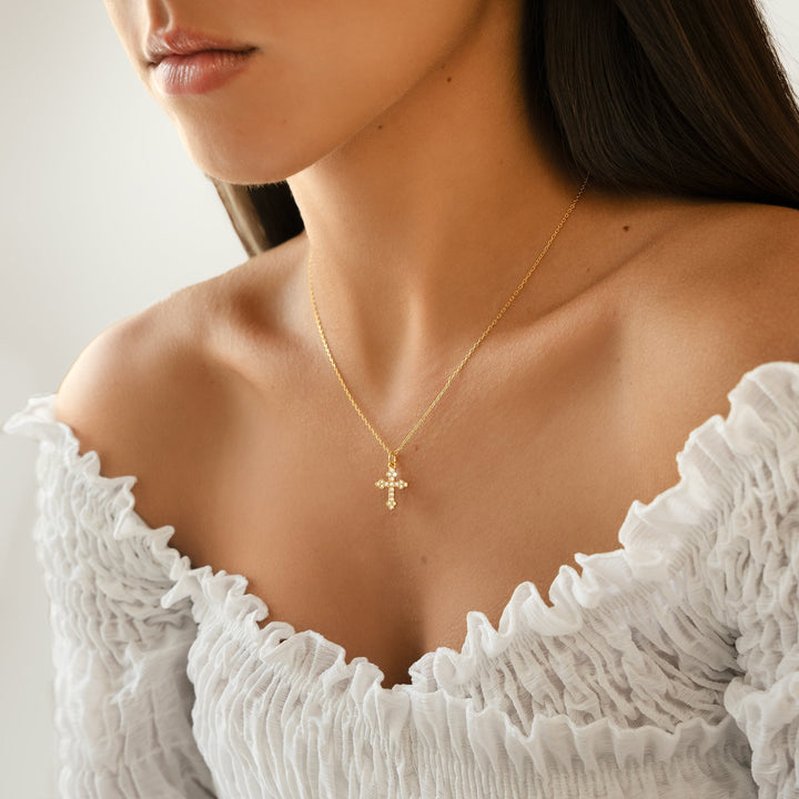 Frau mit goldener Kreuzkette, weißes Kleid, eleganter Schmuck, Nahaufnahme, Modeaccessoire.