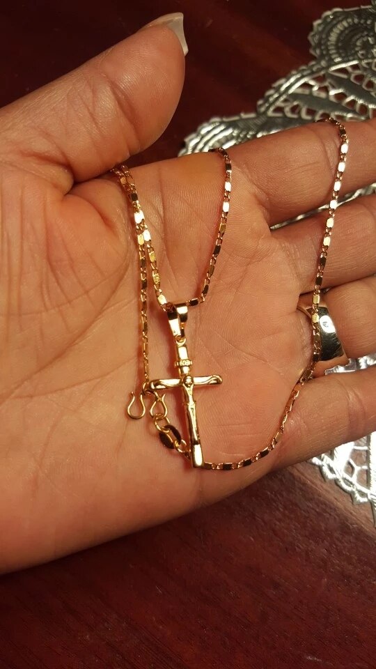 Goldene Kreuzkette in Hand, glänzend, modisches Schmuckstück, religiöses Accessoire.
