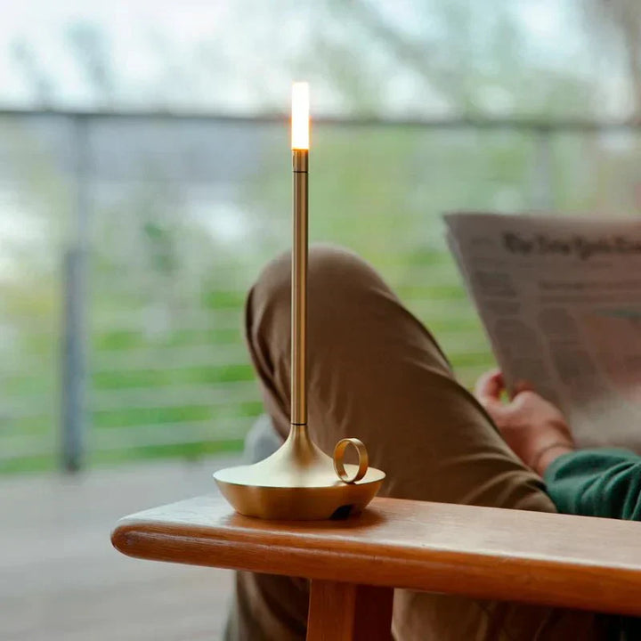 Moderne goldene LED-Tischlampe auf Holzstuhl, ideal für stilvolle Wohnräume.
