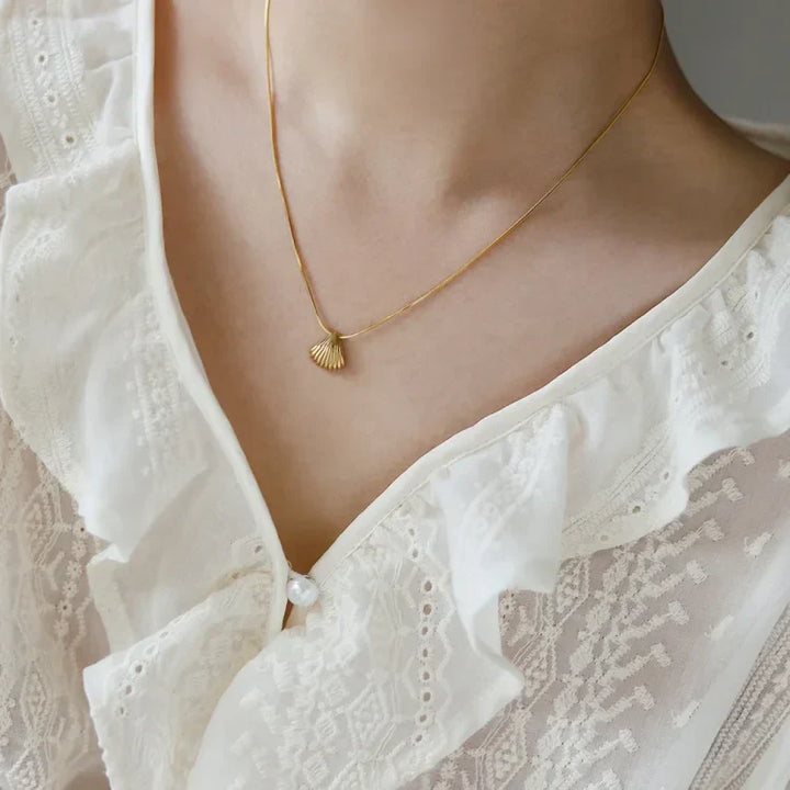 Goldene Muschel-Halskette auf weißer Spitzenbluse, eleganter Schmuck für Damen.