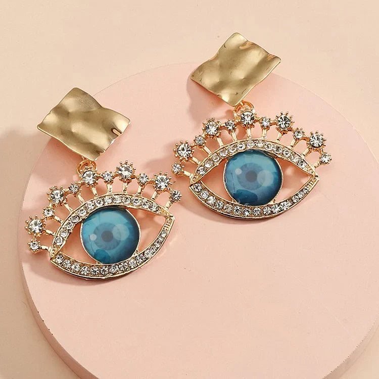 Goldene Ohrringe mit blauem Auge und Strasssteinen, modisches Schmuckdesign, Damenaccessoire.