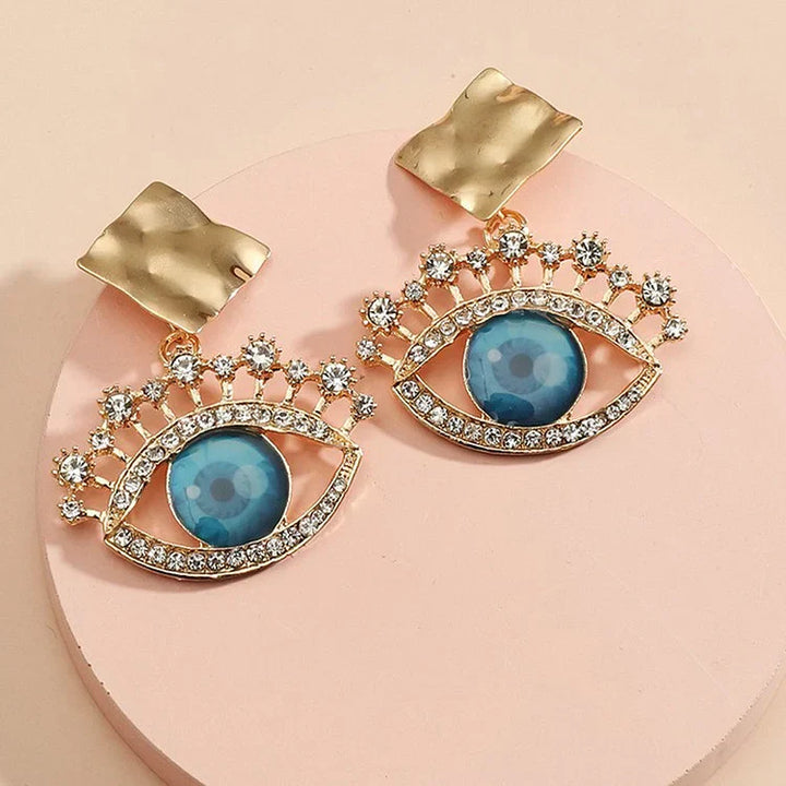 Goldene Ohrringe mit blauem Auge und Strasssteinen, modisches Schmuckdesign, Damenaccessoire.