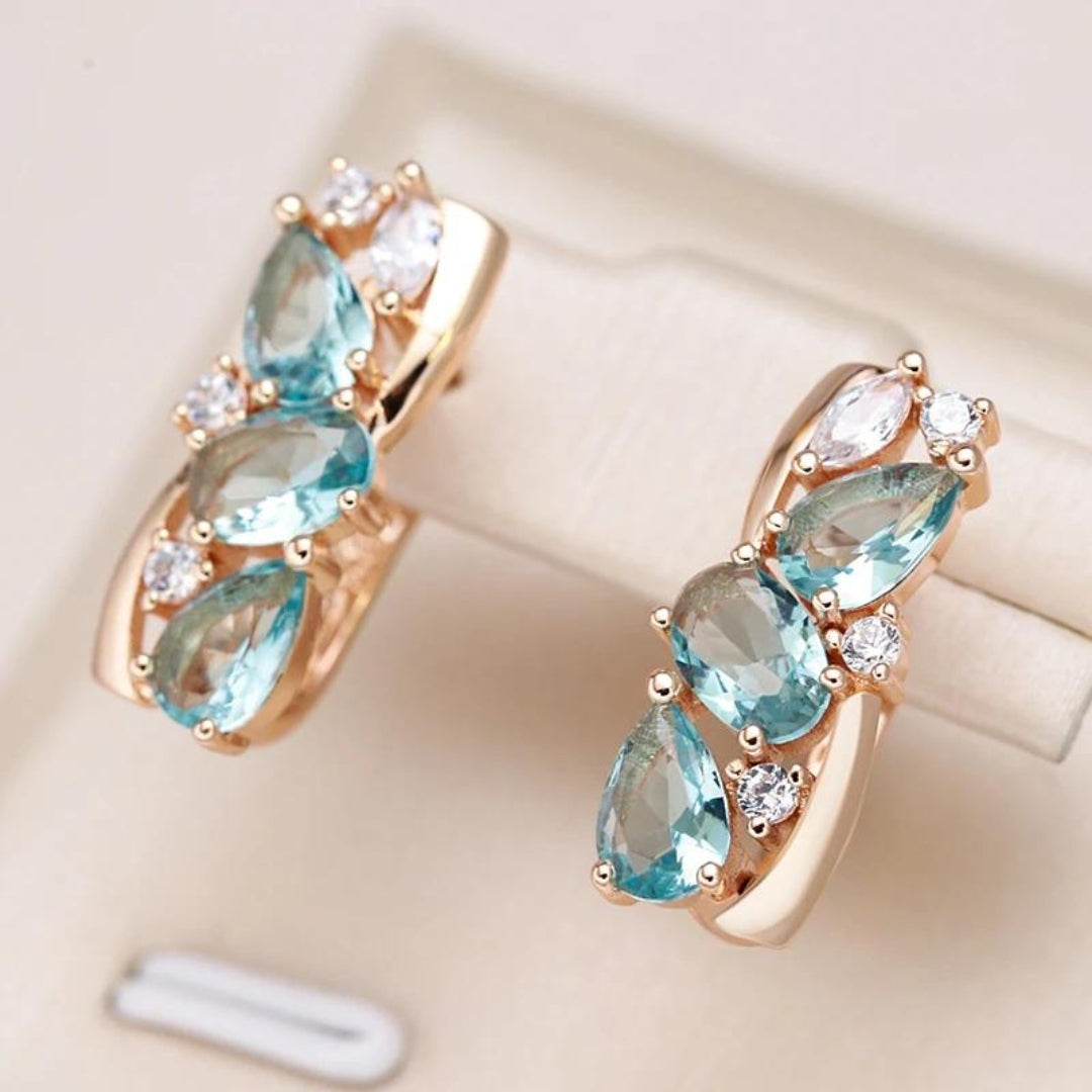 Goldene Ohrringe mit blauen und weißen Edelsteinen, elegantes Schmuckdesign.