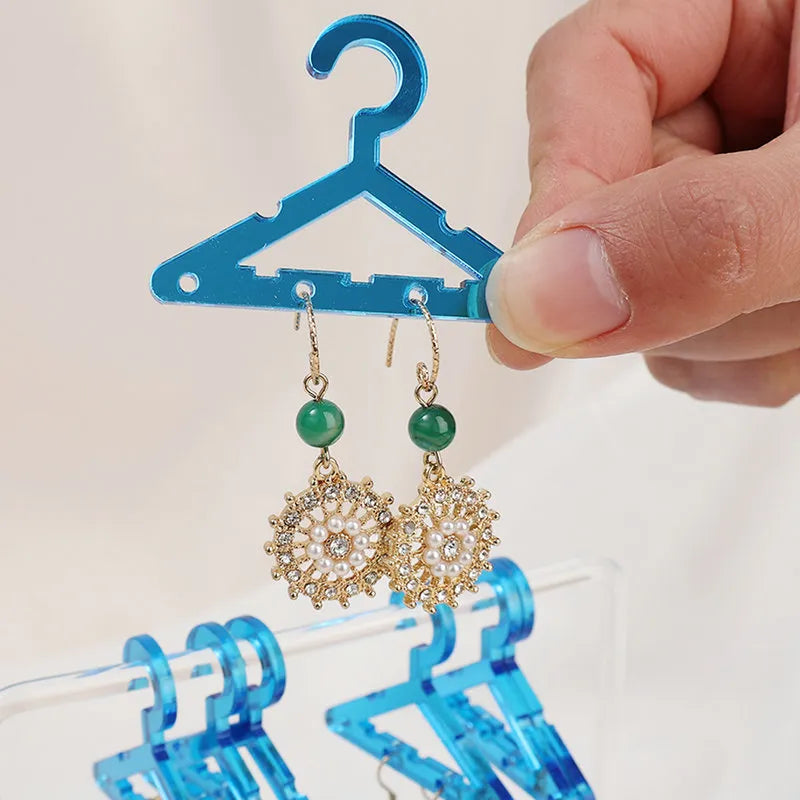 Goldene Ohrringe mit grünen Perlen, hängend an blauem Mini-Kleiderbügel, Schmuckaufbewahrung.