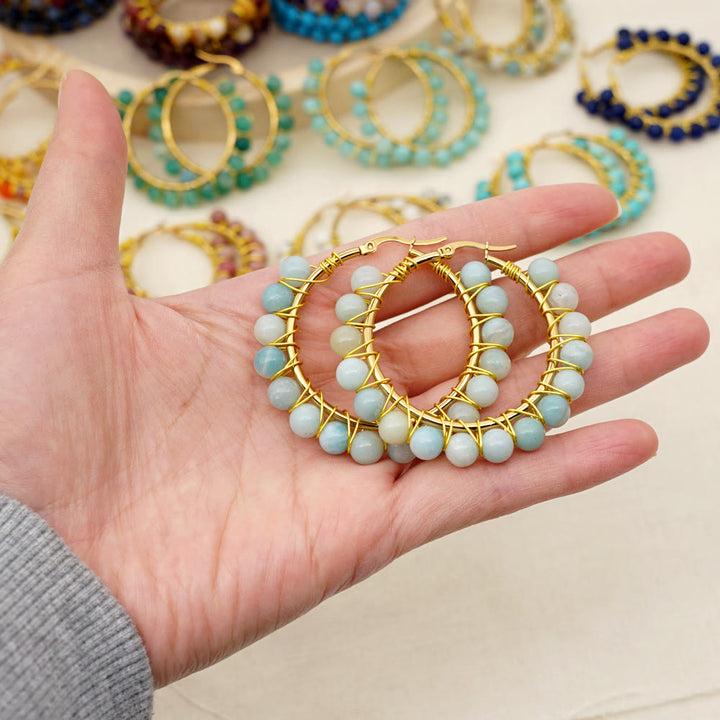 Hand hält goldene Creolen mit blauen Perlen, handgefertigter Schmuck, modische Ohrringe.