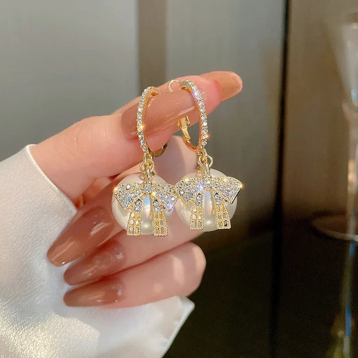 Goldene Ohrringe mit Perlen und Schleifen, funkelnde Strasssteine, eleganter Schmuck.