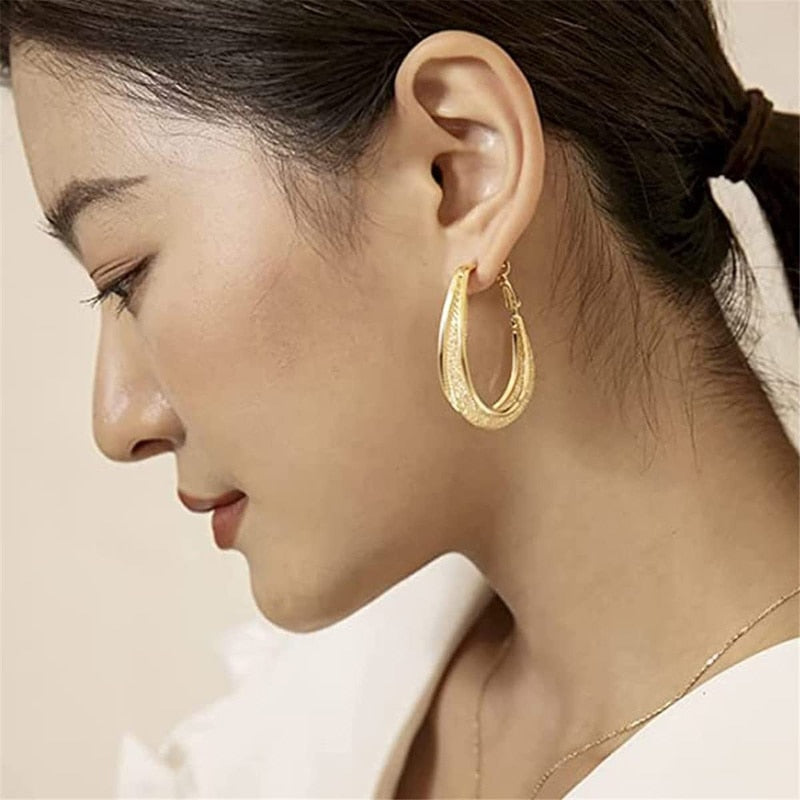 Frau mit goldenen Creolen, eleganter Schmuck, modisches Accessoire, Nahaufnahme, seitliches Profil.