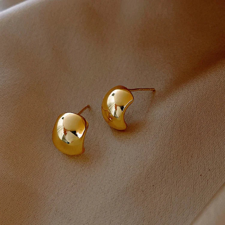 Goldene Ohrringe auf beigem Stoff, elegantes Design, Schmuck, Accessoires, Mode.