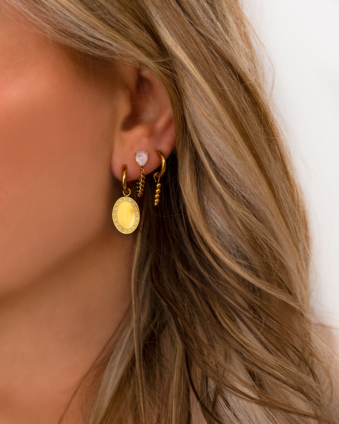 Frau mit goldenen Ohrringen, Herz- und Münzdesign, modischer Schmuck, Nahaufnahme.