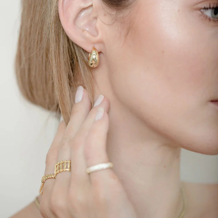 Frau mit goldenen Ohrringen und Ringen, Nahaufnahme, Schmuck, Modeaccessoires, elegantes Design.