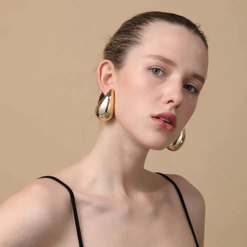 Frau mit goldenen Ohrringen, elegantes Schmuckdesign, Modeaccessoire, stilvolles Aussehen.