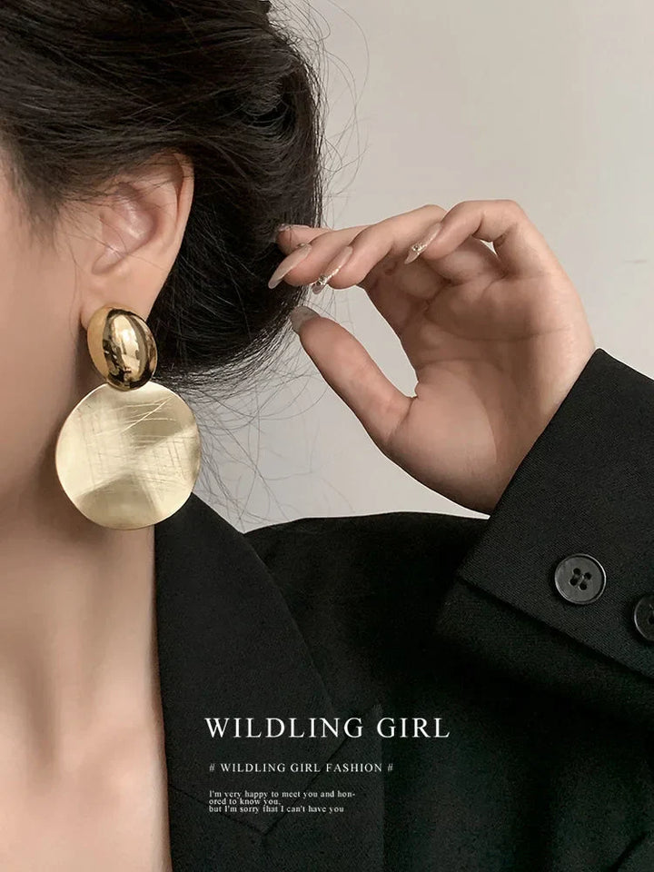Frau mit großen, goldenen Ohrringen und schwarzem Blazer, elegante Modeaccessoires.