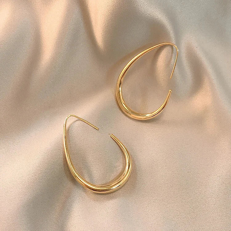 Goldene Creolen Ohrringe auf beigem Satin, eleganter Schmuck, modisches Accessoire.