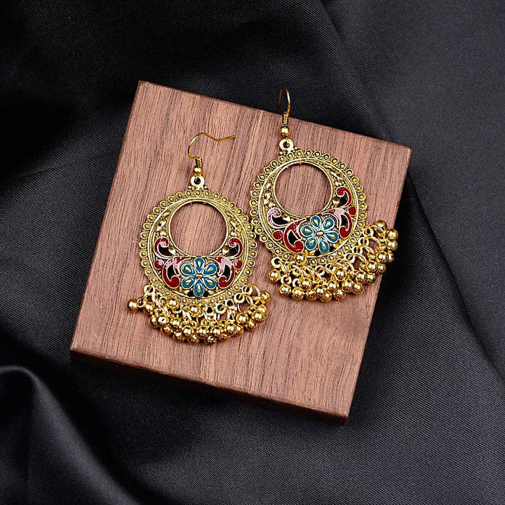 Goldene Ohrringe mit buntem Blumenmuster und Perlen, auf Holzplatte, eleganter Schmuck.