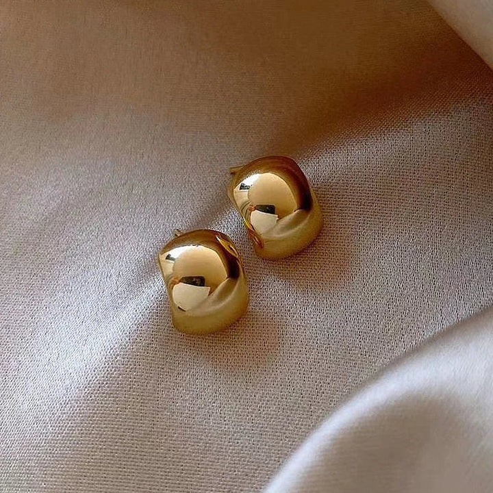 Goldene, glänzende Ohrringe auf beigem Stoff, eleganter Schmuck, modisches Accessoire.
