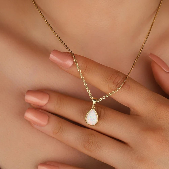 Goldene Halskette mit tropfenförmigem Opal-Anhänger auf Hand, eleganter Schmuck.